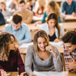 Happy college students cooperating while reading a lecture from papers during a class in the classroom.