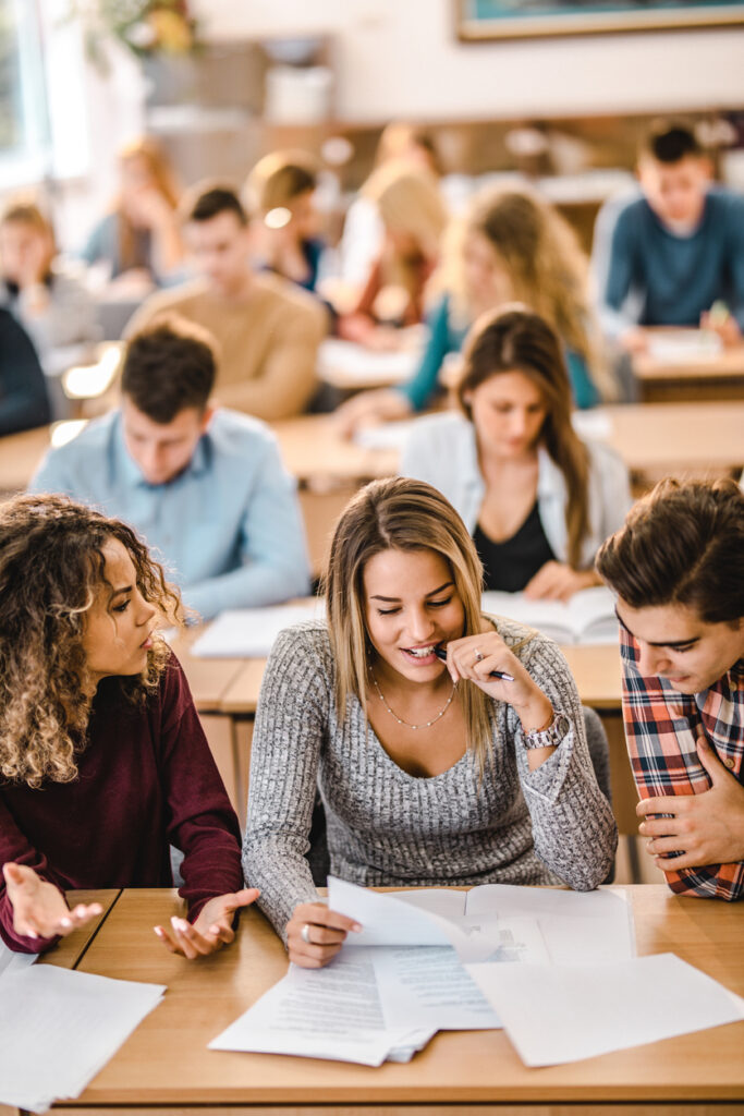 Happy college students cooperating while reading a lecture from papers during a class in the classroom.